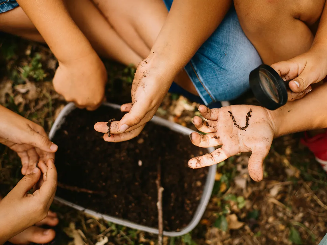 Children exploring soil and a small creature together with a magnifying glass during a hands-on outdoor lesson